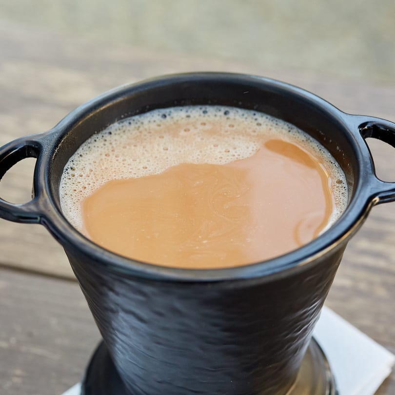 Close-up of a black mug filled with frothy, creamy Indian chai on a wooden table.