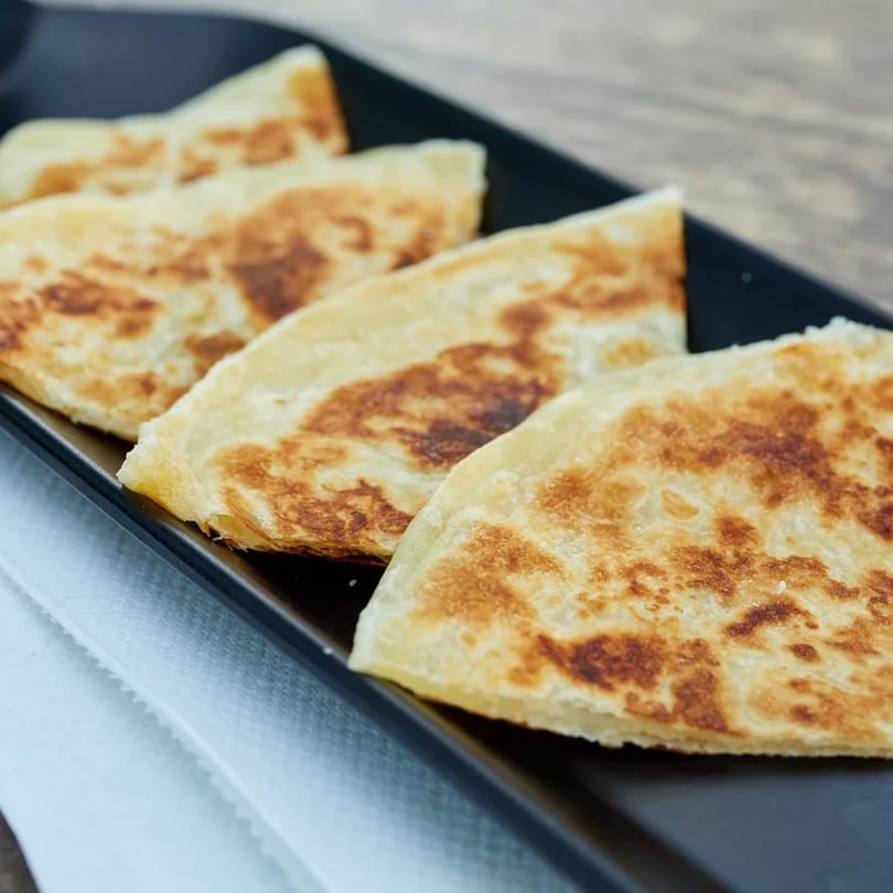 Golden-brown Indian parathas, folded into triangles, arranged on a black rectangular plate.