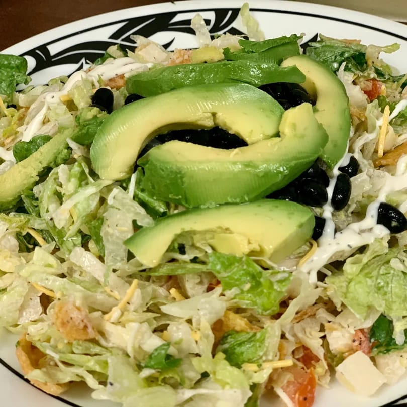 A fresh salad with sliced avocado, black beans, lettuce, and a creamy dressing on a white plate.